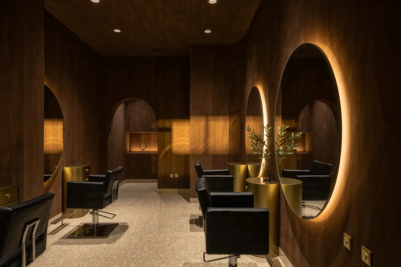 Intérieur du salon : boiseries chocolat, miroirs ronds rétroéclairés, fauteuils en cuir noir et détails en laiton